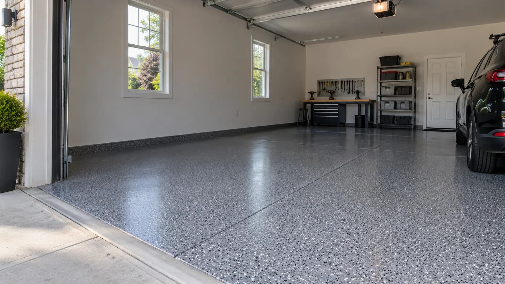 Illustrative residential garage with a grey flake floor coating, an open door, and part of a vehicle.